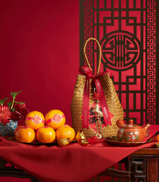 Woven straw basket with red ribbons, gold horse charm, fresh mandarin oranges, gold ingots, and traditional ceramics for