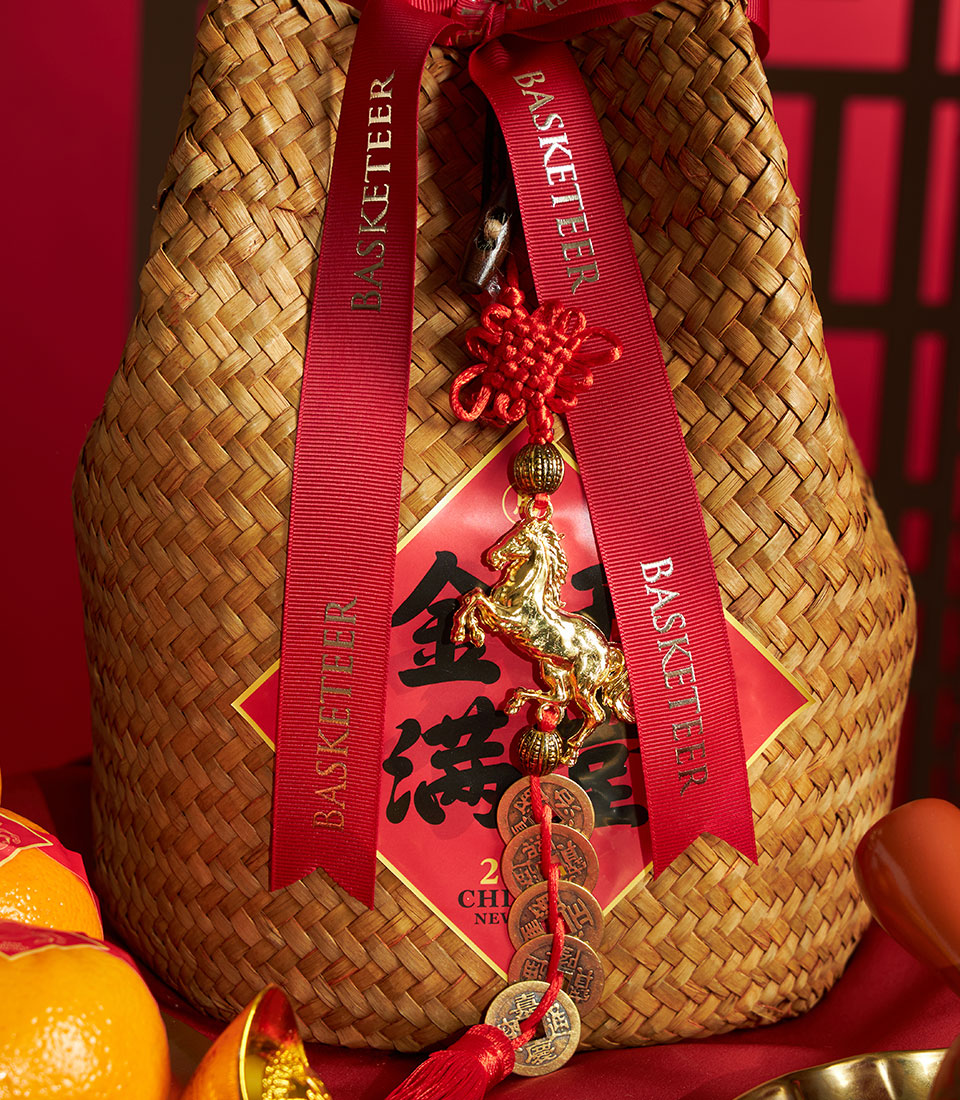 Woven straw gift basket with mandarin oranges, red ribbons, Chinese knot charm, and gold coins for Chinese New Year