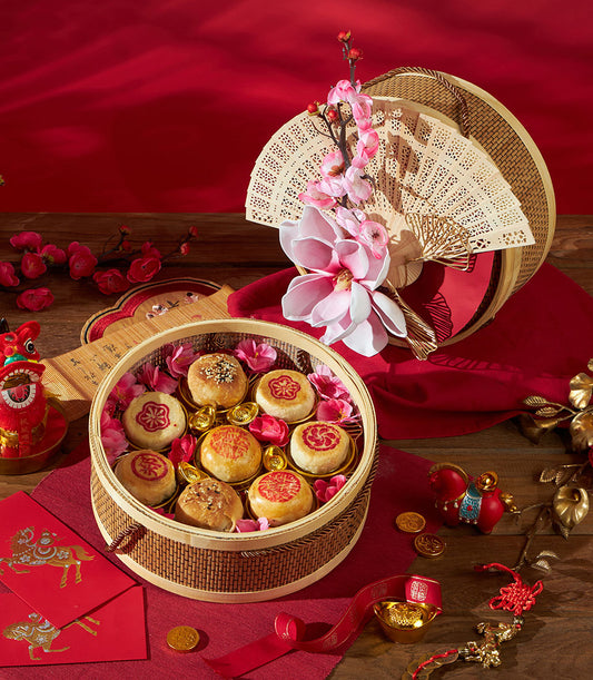 Festive Chinese New Year pastry gift basket with sesame and red-stamped baked goods, gold ingots, cherry blossoms, and
