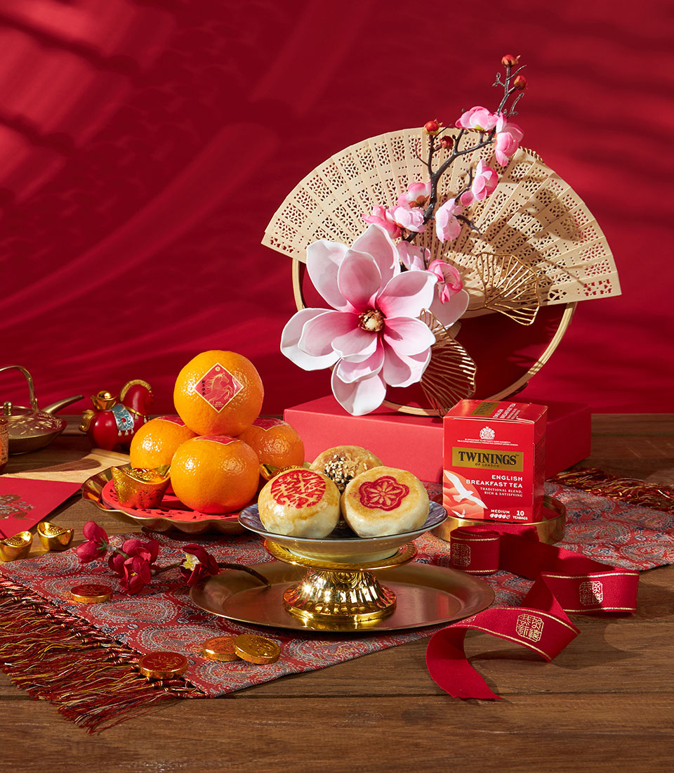 Mandarin oranges, tea, and pastries in festive red and gold Chinese New Year gift set with cherry blossoms