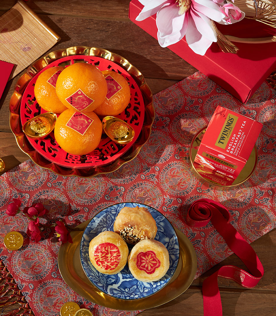 Festive mandarin oranges with gold ingots, tea, pastries, and red accents for Chinese New Year gifting