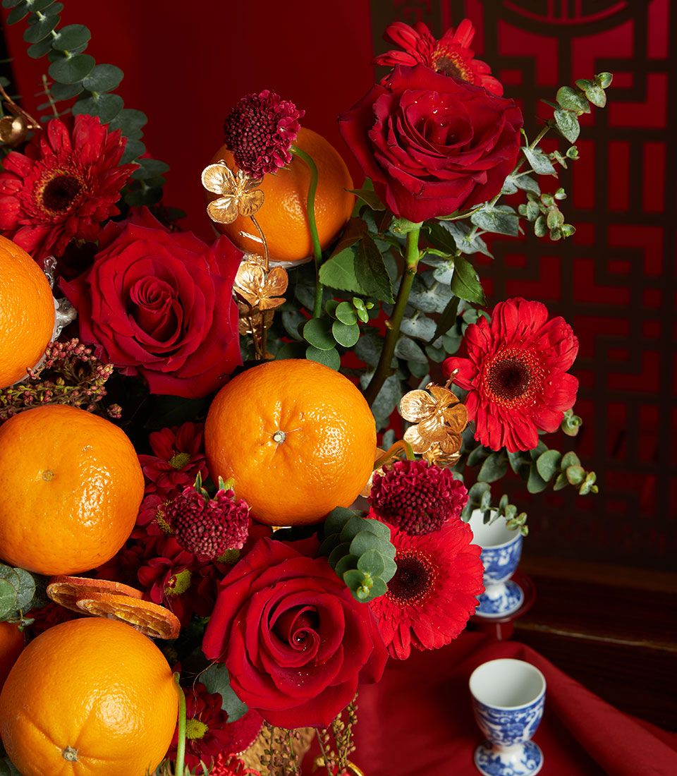 Vibrant mandarin orange and red rose floral arrangement with gold accents for Chinese New Year gifting