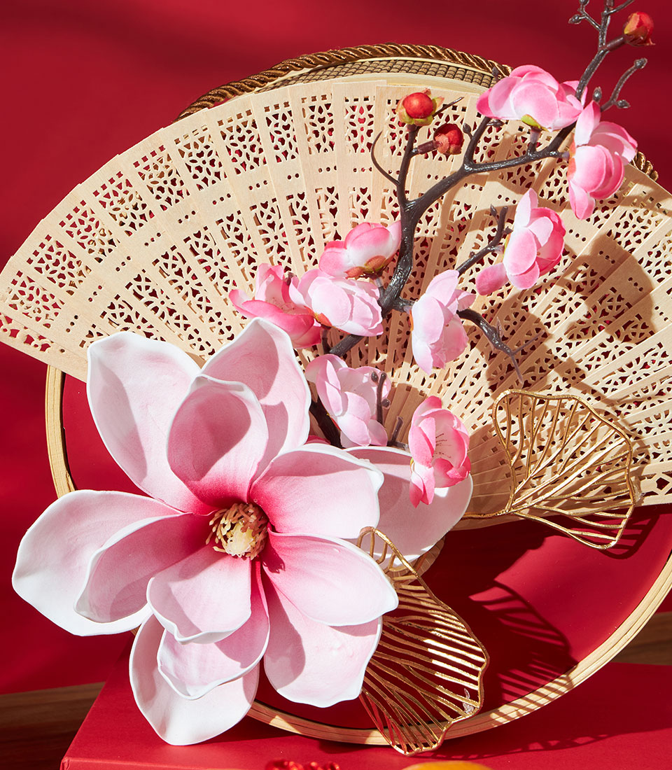 Luxury mandarin orange gift basket with carved bamboo fan, pink magnolia flowers, and golden accents for Chinese New Year