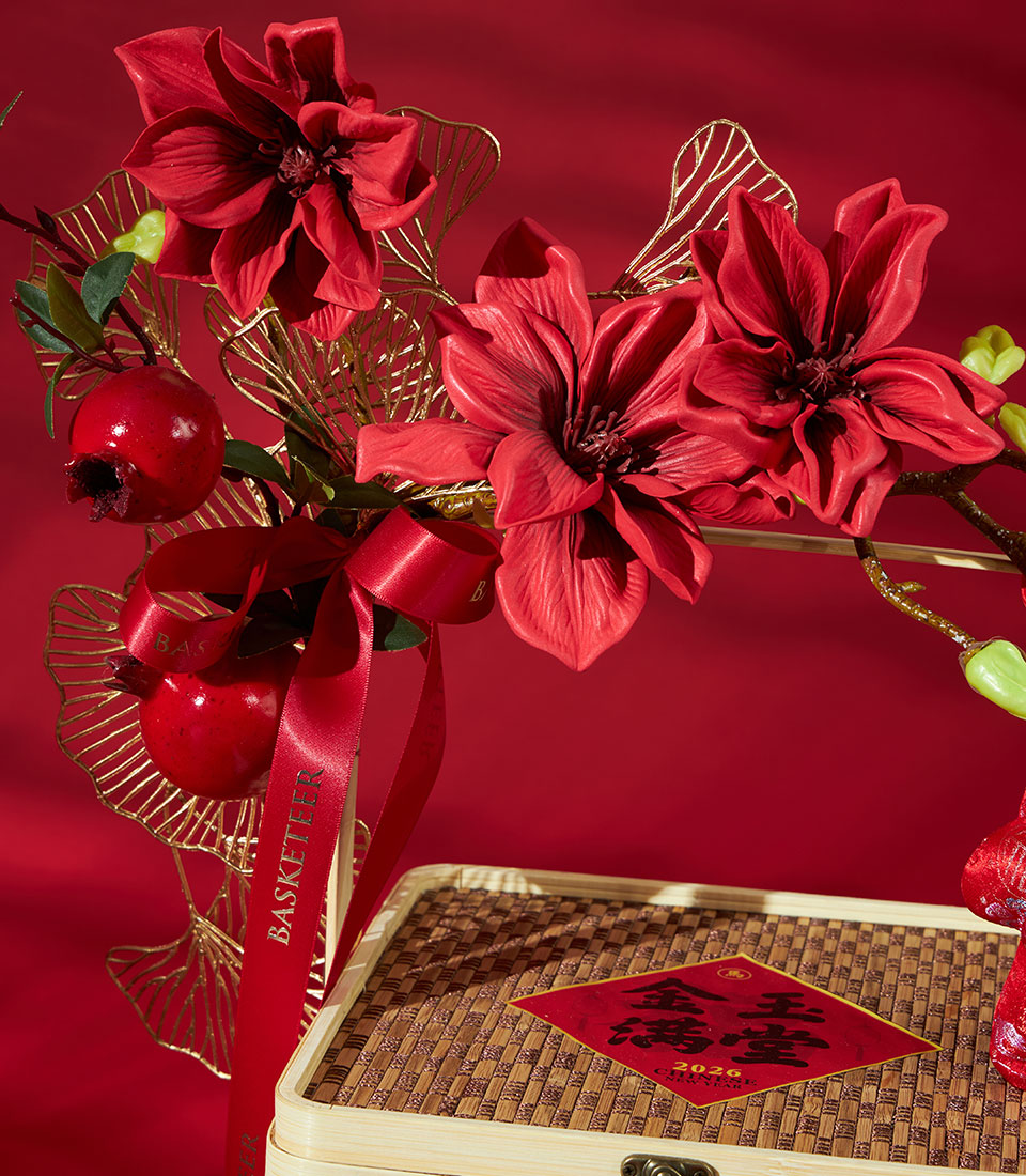 Festive red and gold Chinese New Year gift hamper with magnolia flowers, pomegranates, and mandarin oranges in woven bamboo