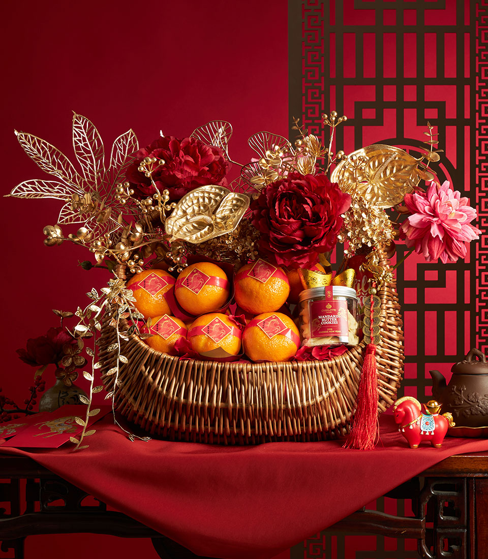 Wicker basket with mandarin oranges, red peonies, gold accents, and cookies for Chinese New Year gifting