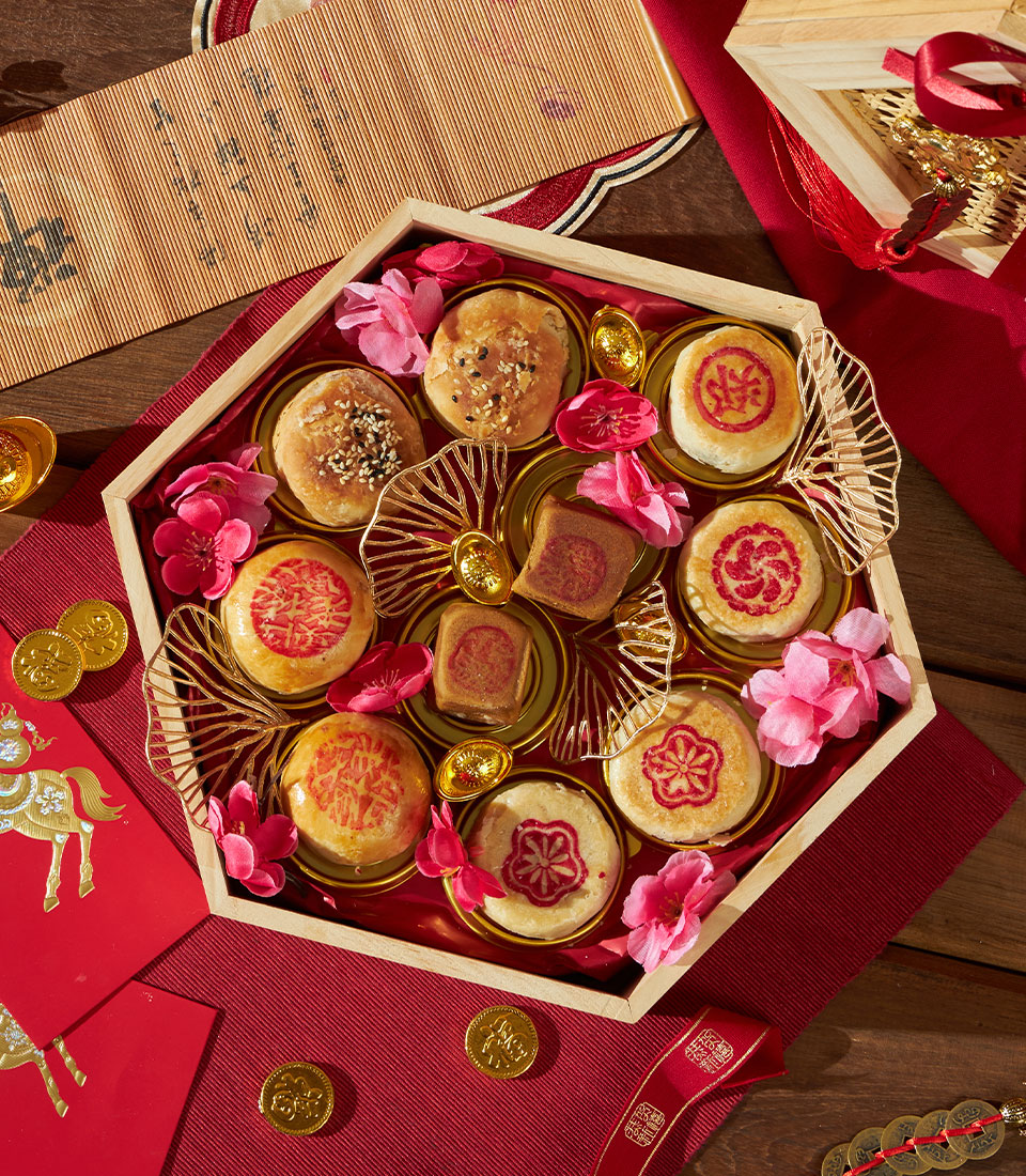 Hexagonal wooden gift box with assorted Chinese pastries, golden stands, and festive cherry blossom decorations for Lunar