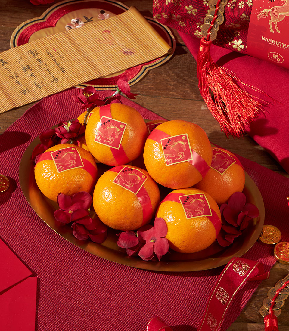 Festive gold tray with mandarin oranges tied in red ribbons, red flowers, and Chinese New Year auspicious symbols