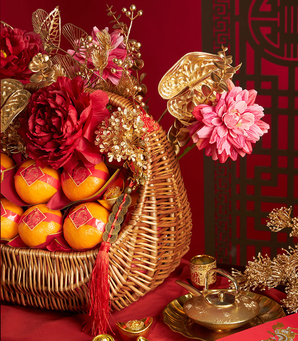 Festive wicker basket overflowing with red-wrapped mandarin oranges, gold accents, and red flowers for Chinese New Year