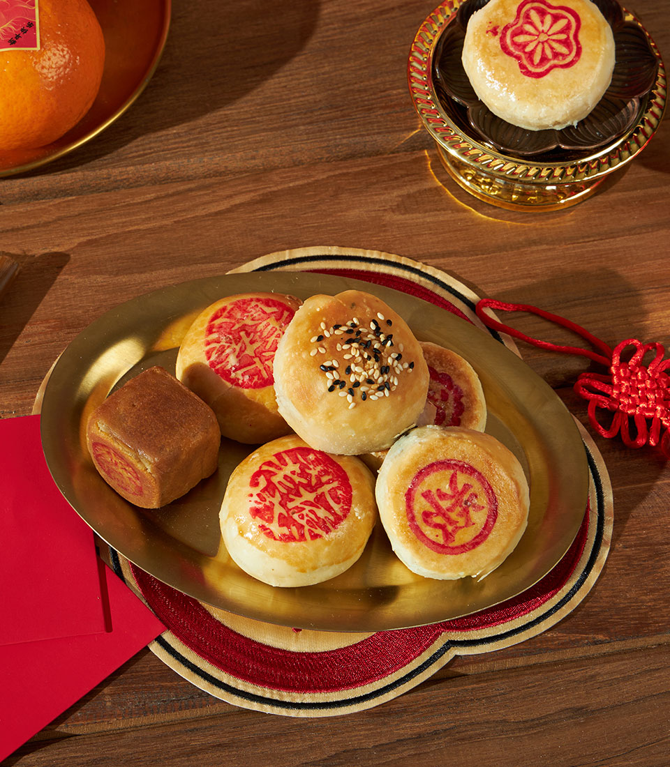 Chinese New Year mandarin and pastry gift set with sesame treats, red envelopes, and gold serving platters on embroidered mat