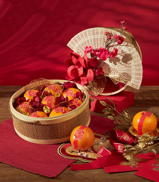 Festive mandarin orange gift basket with red and gold labels, decorative fans, and lucky ornaments for Chinese New Year