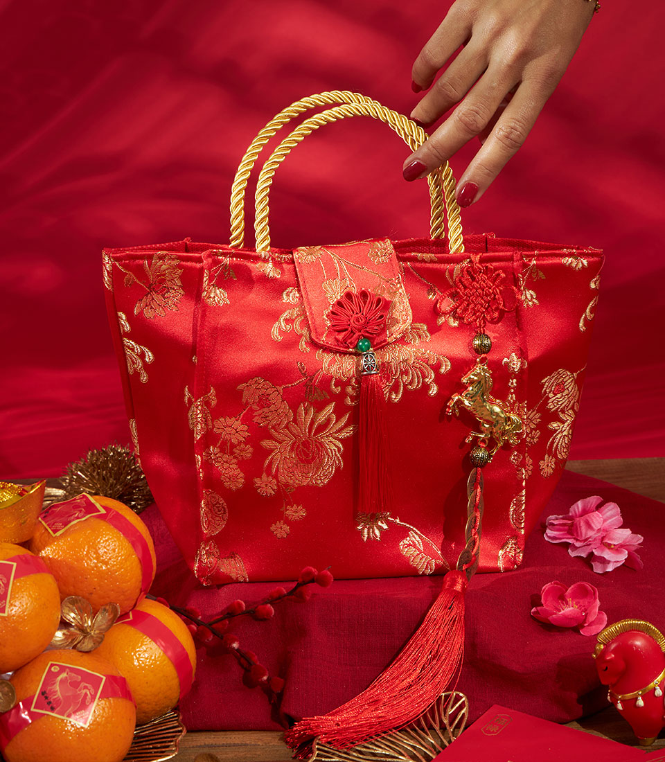 Red satin mandarin orange gift bag with gold embroidery, braided handles, and lucky charms for Chinese New Year