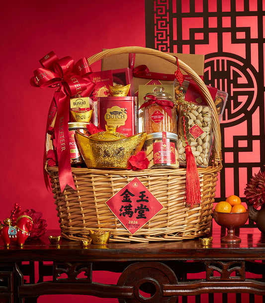 Wicker gift basket with red satin bow filled with gourmet treats, gold ingots, and mandarin oranges for Chinese New Year