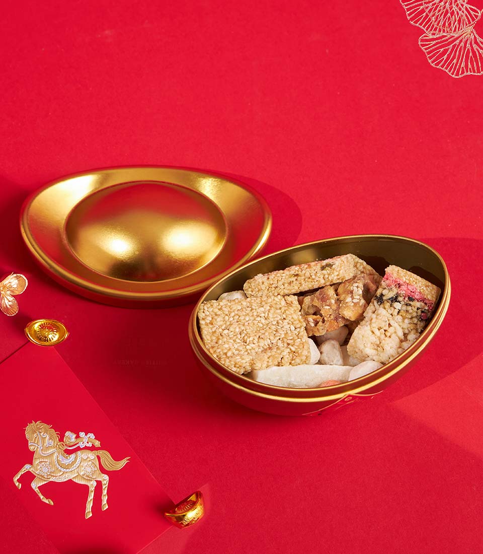 Golden sycee container filled with sesame brittle and festive sweets, red hongbao envelope, Chinese New Year gift set