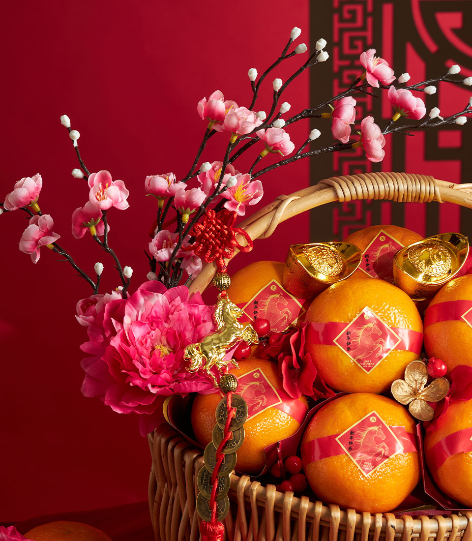Woven wicker basket filled with red-banded mandarin oranges, gold ingots, and pink peonies with red Chinese knot for Lunar