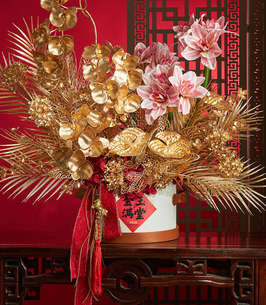 Basketeer: A luxurious Chinese New Year gift with golden orchids, palm fronds, and pink amaryllis. Red and gold ribbon adds warmth to this premium hamper.