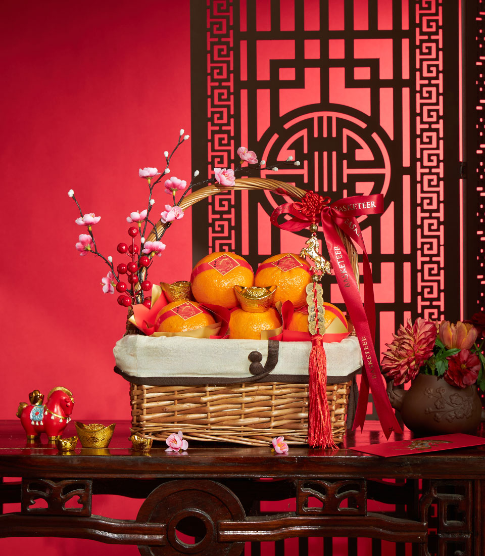 Festive Chinese New Year mandarin orange gift basket with gold ingots, plum blossoms, and lucky charms on red background