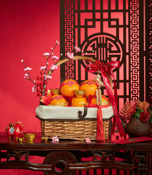 Festive Chinese New Year mandarin orange gift basket with gold ingots, plum blossoms, and lucky charms on red background
