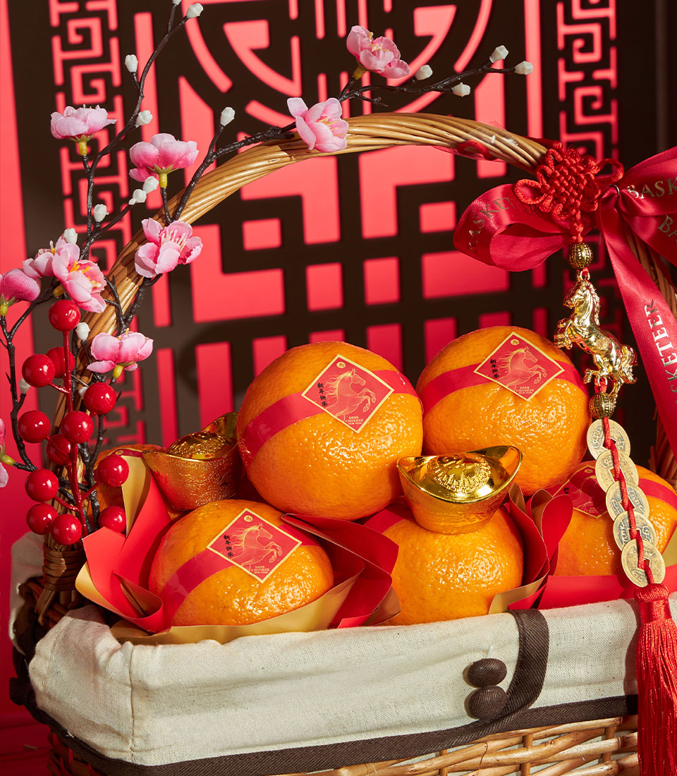Woven wicker Chinese New Year mandarin orange gift basket with golden ingots, cherry blossoms, and red ribbon charm