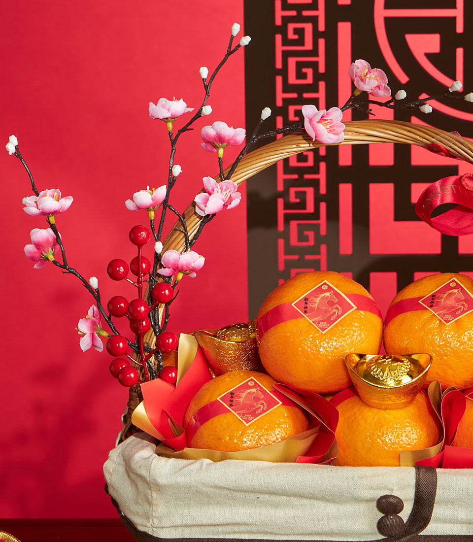 Festive Chinese New Year mandarin orange gift basket with woven trim, red ribbons, gold ingots, and cherry blossom branches