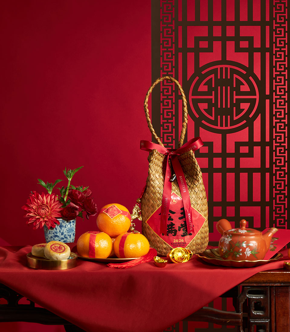 Woven straw gift basket with red satin ribbons, mandarin oranges, red flowers, ceramic teapot, and gold accents for Chinese