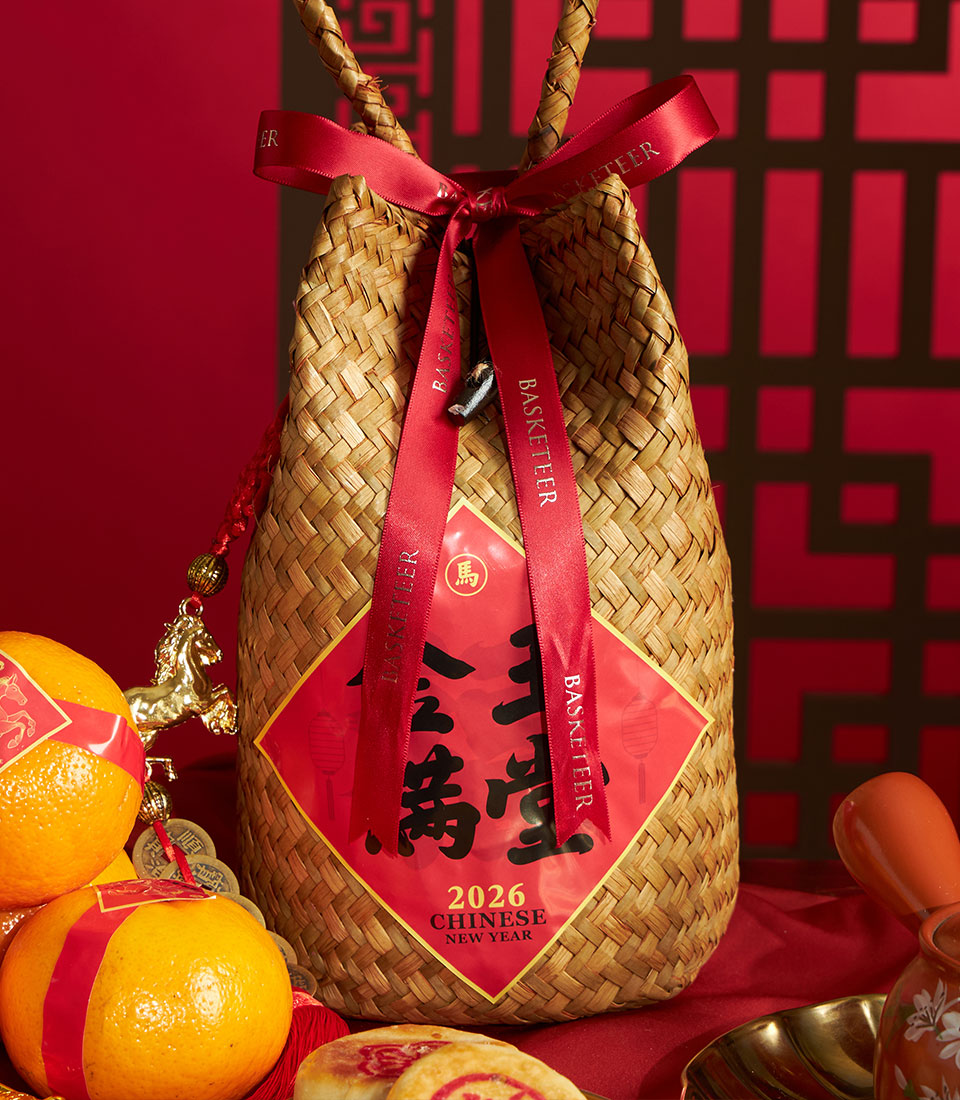 Woven straw Chinese New Year gift basket with mandarin oranges, red ribbons, ceramic pot, and traditional charms