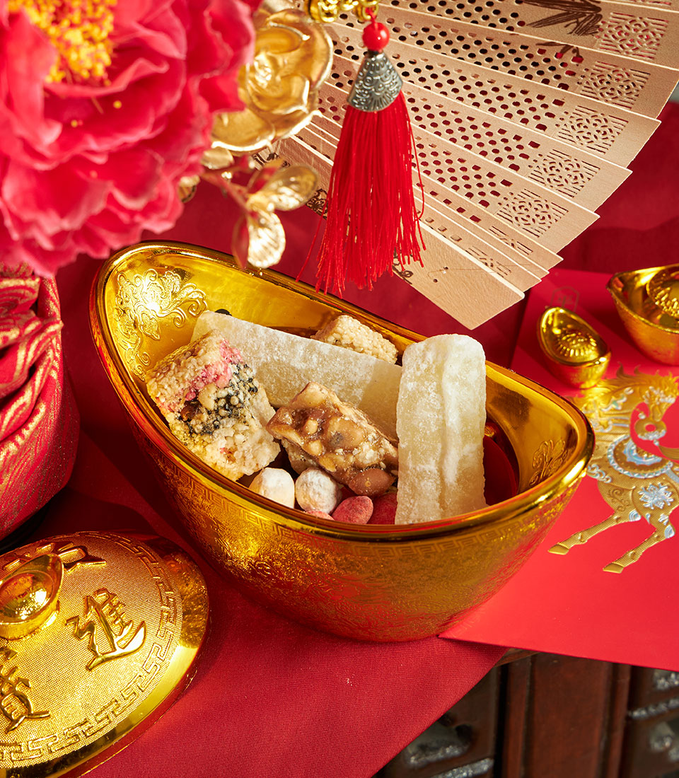 Luxury Chinese New Year gift set with golden yuanbao container, premium candies, red peony, carved wooden fan, and lucky red