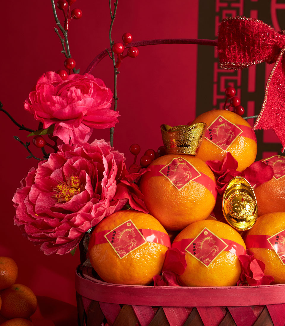 Festive Chinese New Year mandarin orange basket with pink peonies, red berries, and gold ingot decorations