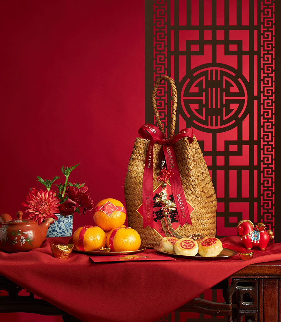 Woven straw gift basket with mandarin oranges, pastries, and festive red ribbons for Chinese New Year