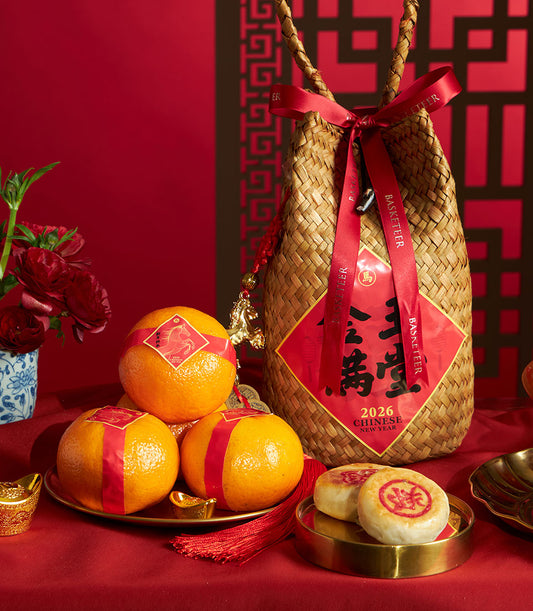 Woven straw gift basket with mandarin oranges, pastries, and red silk ribbons for Chinese New Year celebration