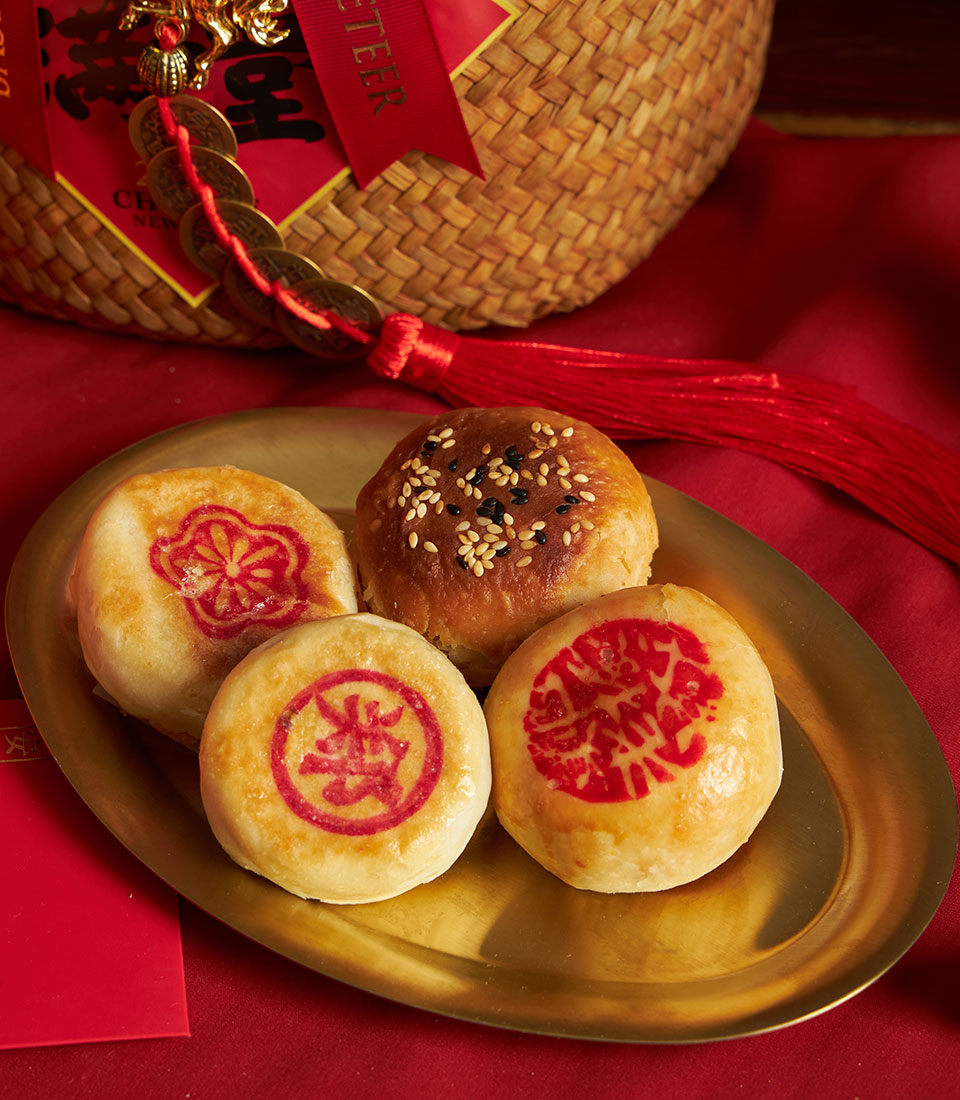 Chinese New Year pastries and mandarin oranges in golden tray with red silk, lucky coins, and woven basket