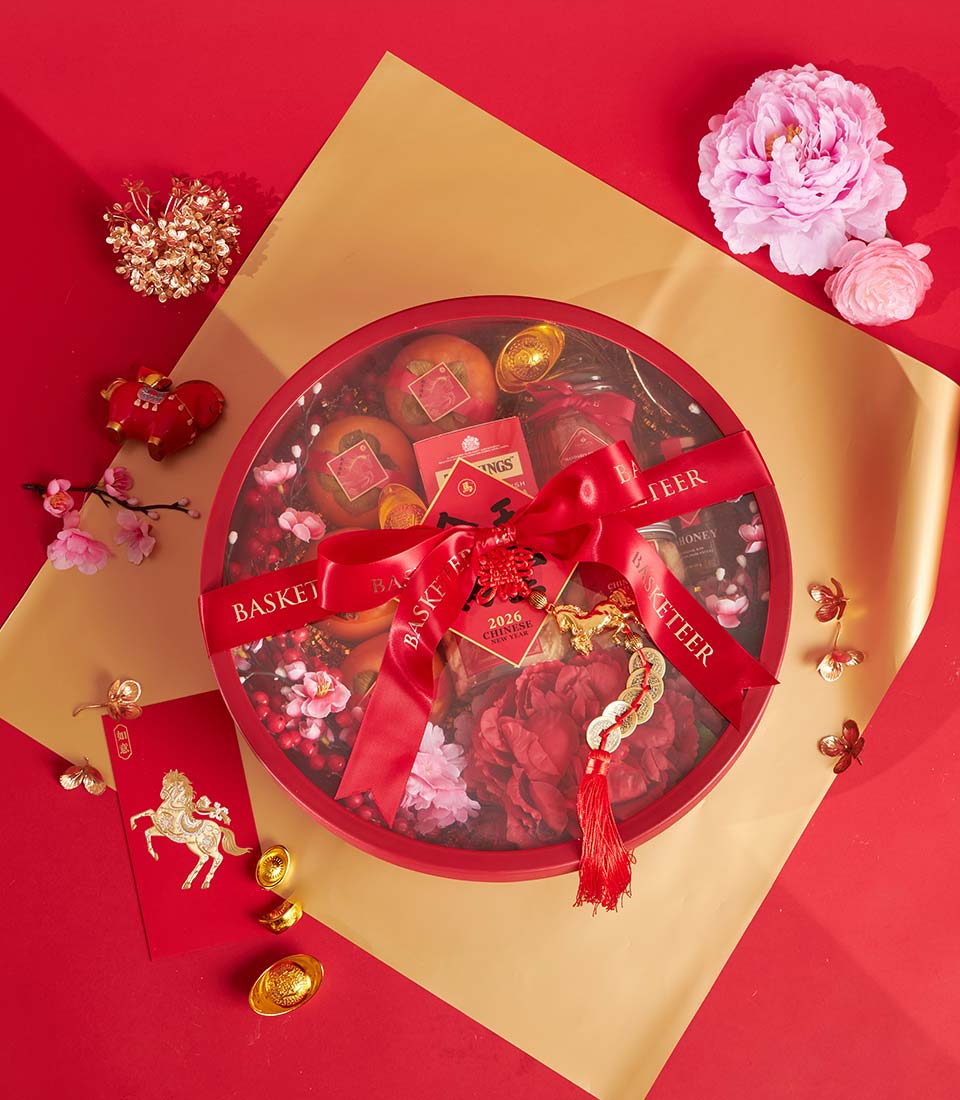 Circular gift basket with persimmons, tea, and honey jars tied with red ribbon on festive red and gold Chinese New Year