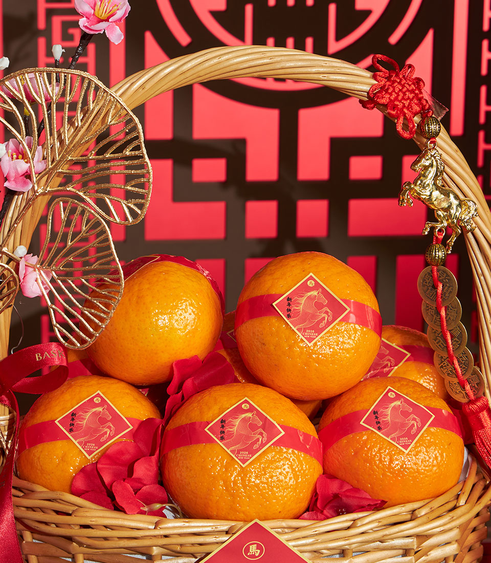 Wicker basket of mandarin oranges with red ribbons, golden horse charms, and pink cherry blossoms for Chinese New Year