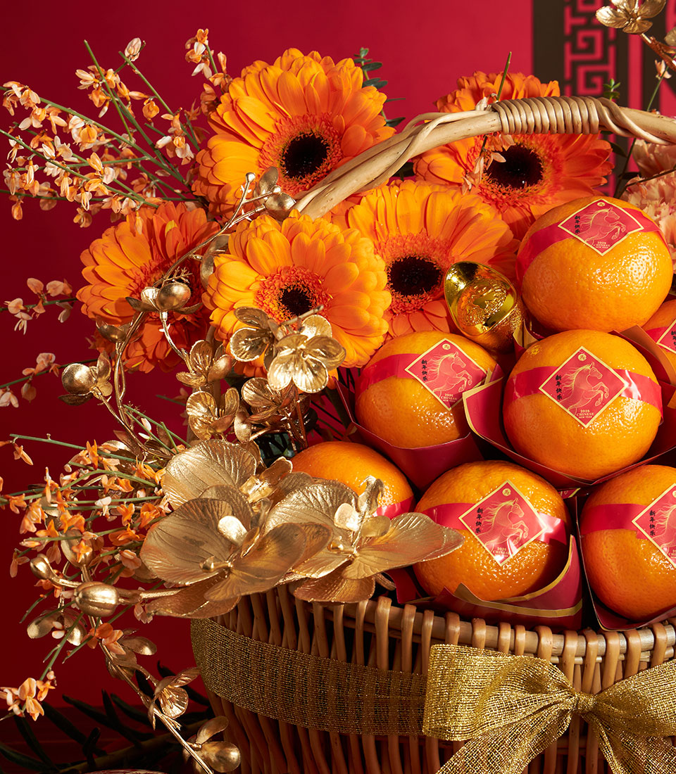 Woven wicker basket with mandarin oranges in red wrapping and golden gerbera daisies for Chinese New Year gifting