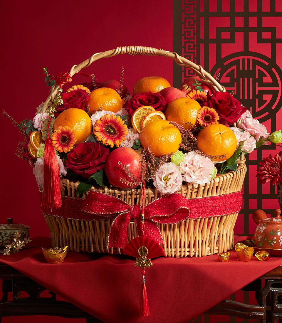 Wicker basket with fresh roses, gerberas, and carnations alongside mandarins, pomegranates, and dried citrus for Chinese New