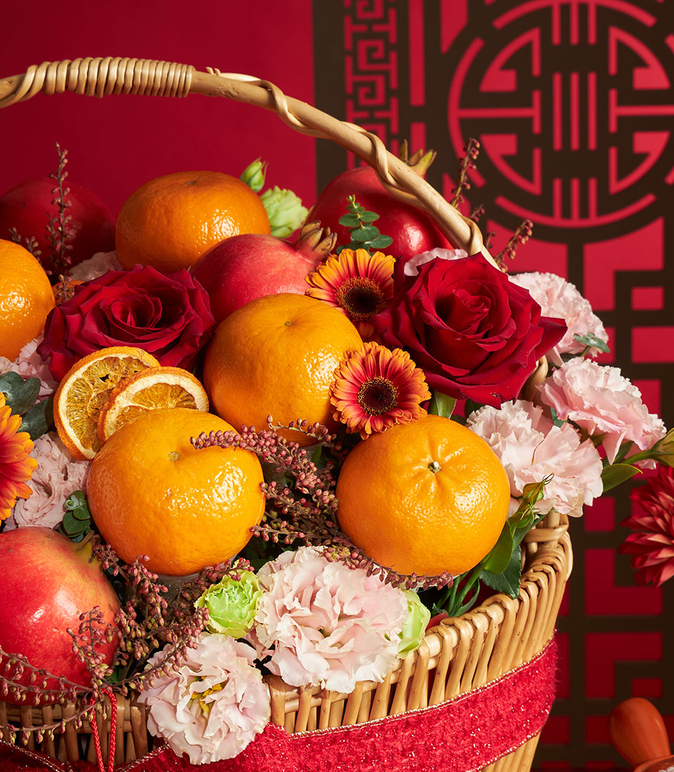 Chinese New Year fresh fruit and flower basket with tangerines, pomegranates, red roses and gerbera daisies in woven wicker
