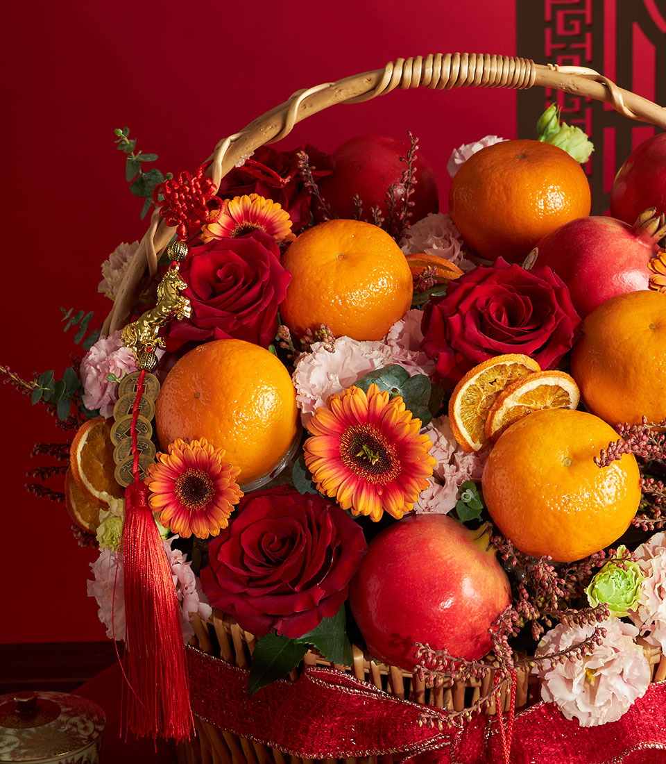 Chinese New Year fruit and flower gift basket with oranges, pomegranates, red roses, and gerberas in woven wicker
