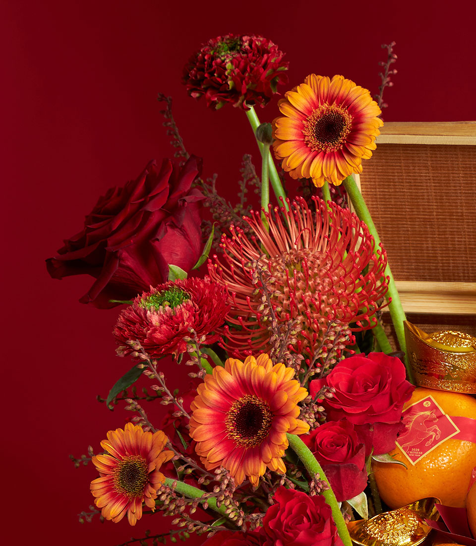 Red and orange flower arrangement with fresh mandarin oranges and gold accents for Chinese New Year