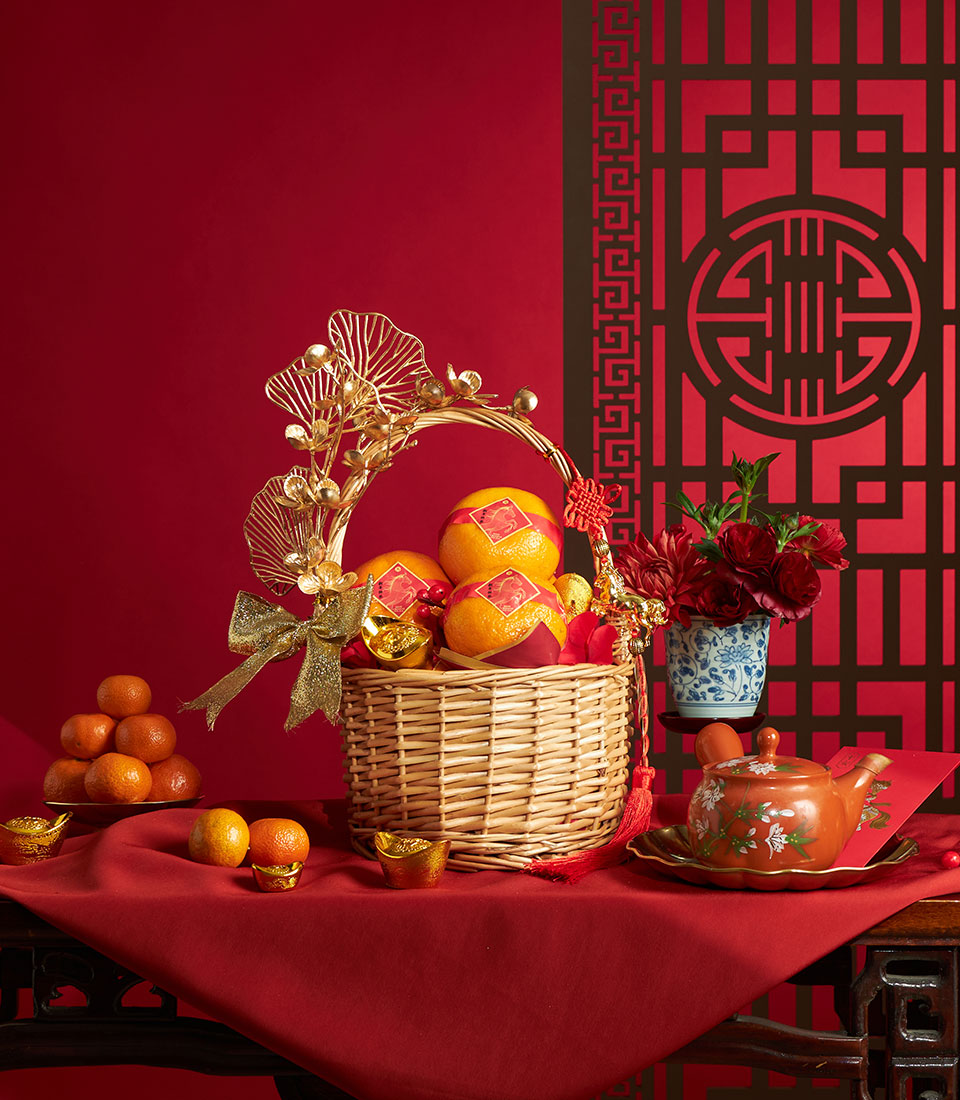 Festive Chinese New Year mandarin orange gift basket with gold accents, red tassel bow, and ceremonial ornaments on red