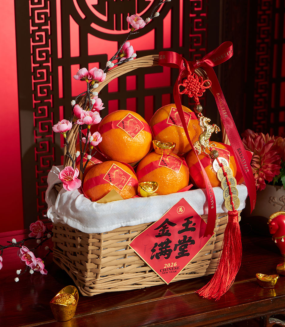 Woven wicker basket filled with bright mandarin oranges, gold ingots, and cherry blossoms tied with red ribbon and Chinese