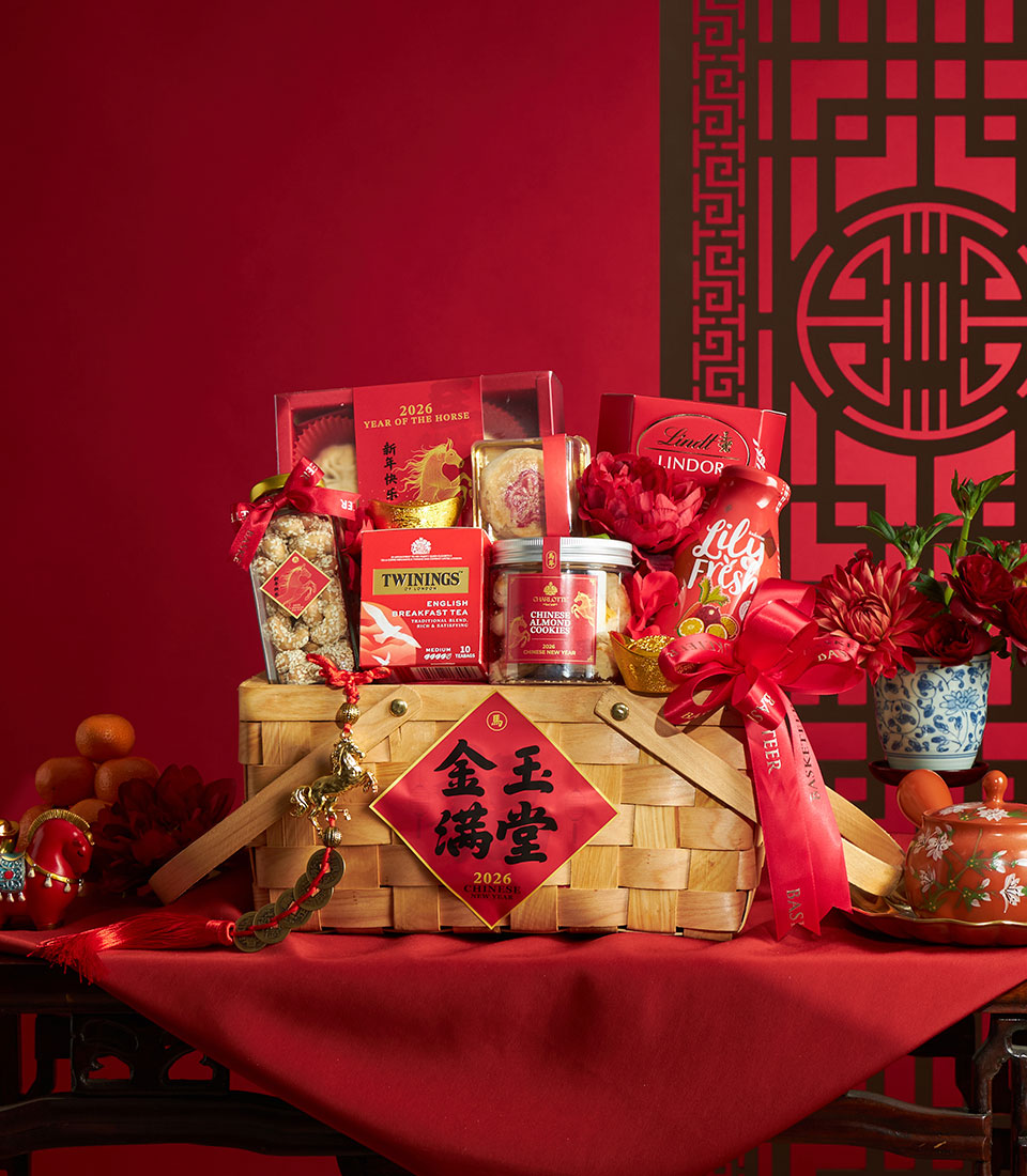 Woven gift basket filled with premium treats, tea, and gourmet goods, decorated with red peonies and gold accents for