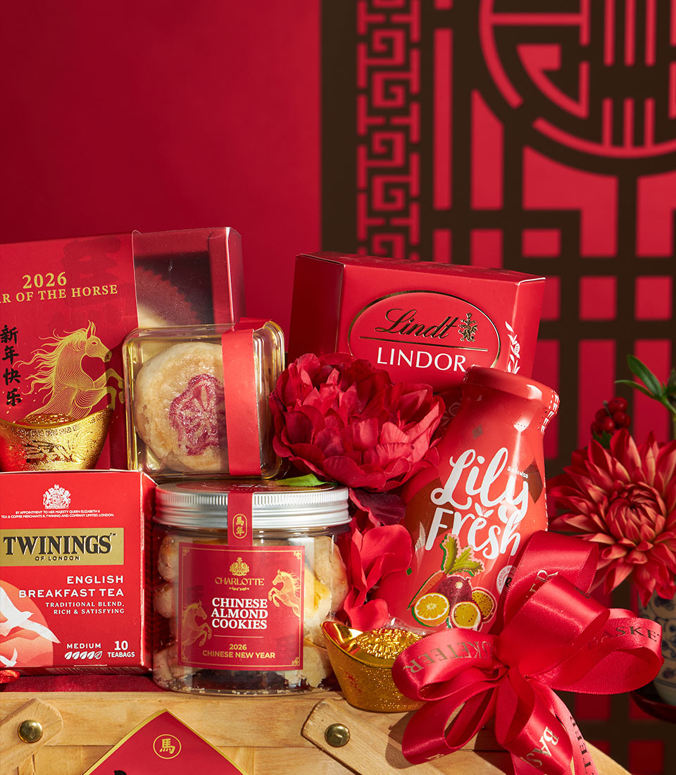 Festive Chinese New Year gourmet gift basket with chocolates, almond cookies, tea, and red ribbon on crimson background