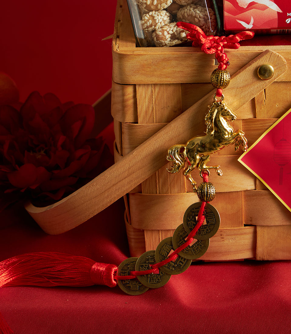 Festive Chinese New Year gourmet gift basket with sesame snacks, gold horse charm, and red silk cord on woven wooden base