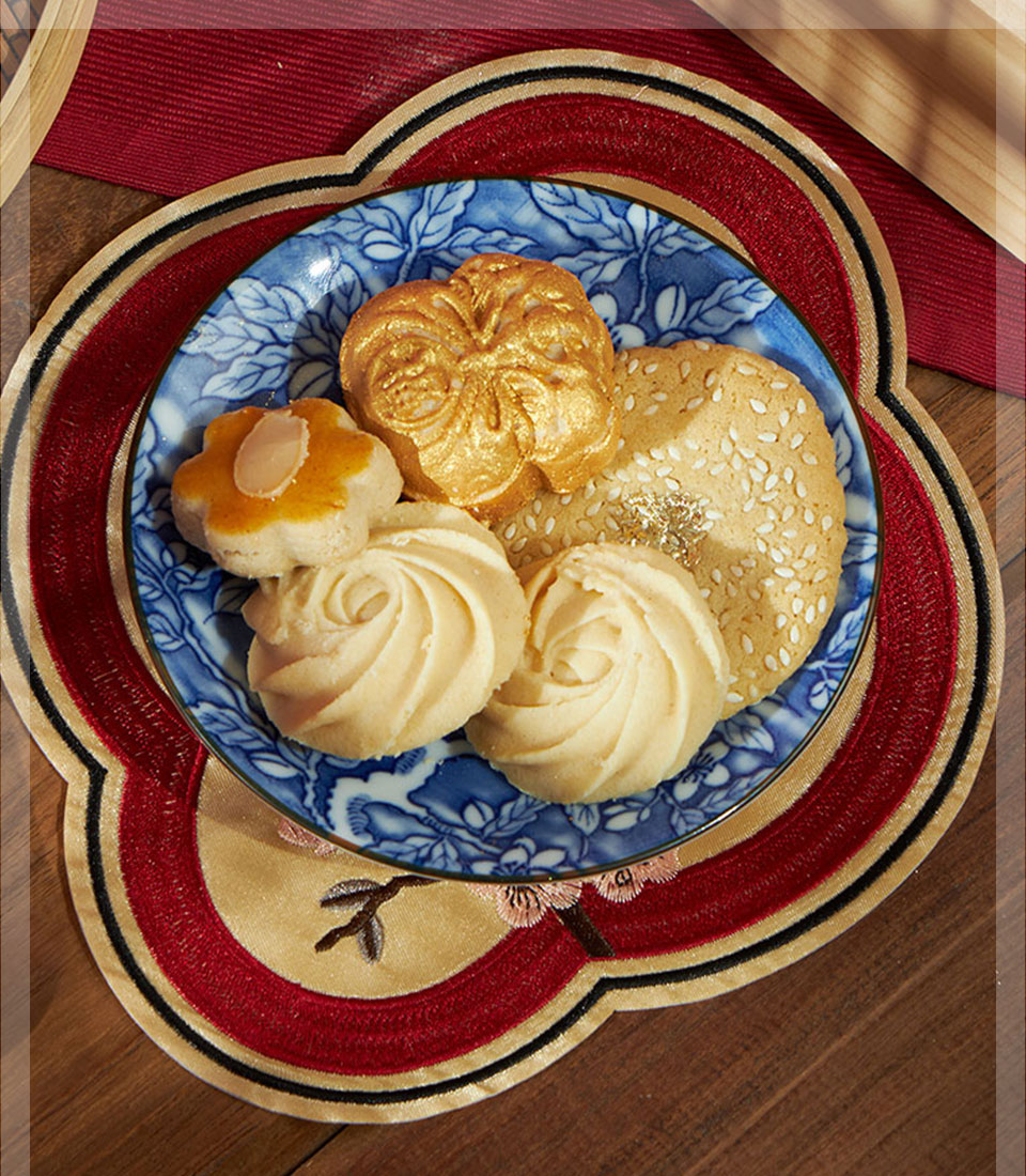 Prosperity Assorted Cookies gift set with golden molded cookie, flower-shaped almond cookie, and sesame seed cookies on blue