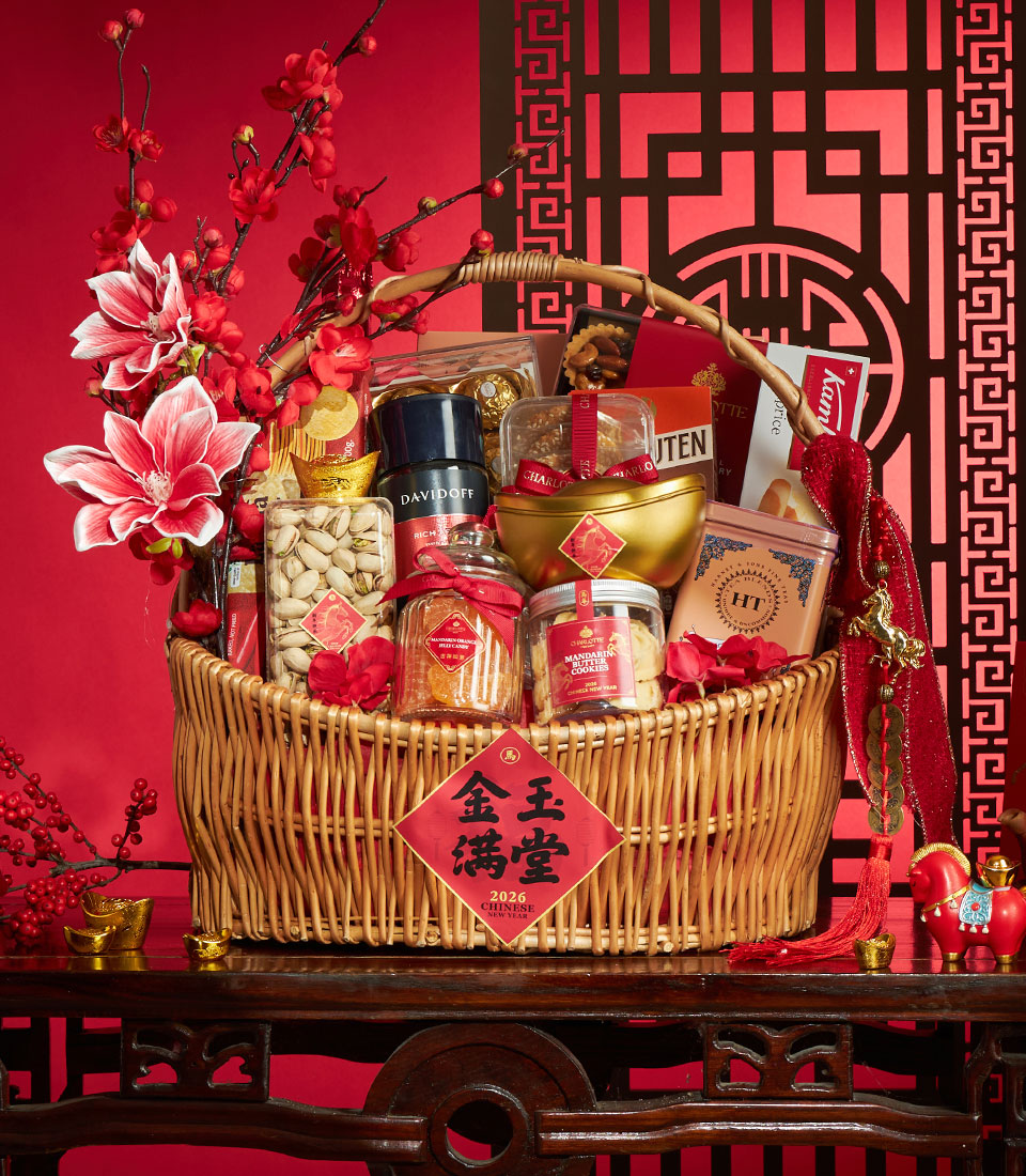 Woven wicker Chinese New Year gift basket with gourmet snacks, golden ingots, and festive red ribbons on red patterned
