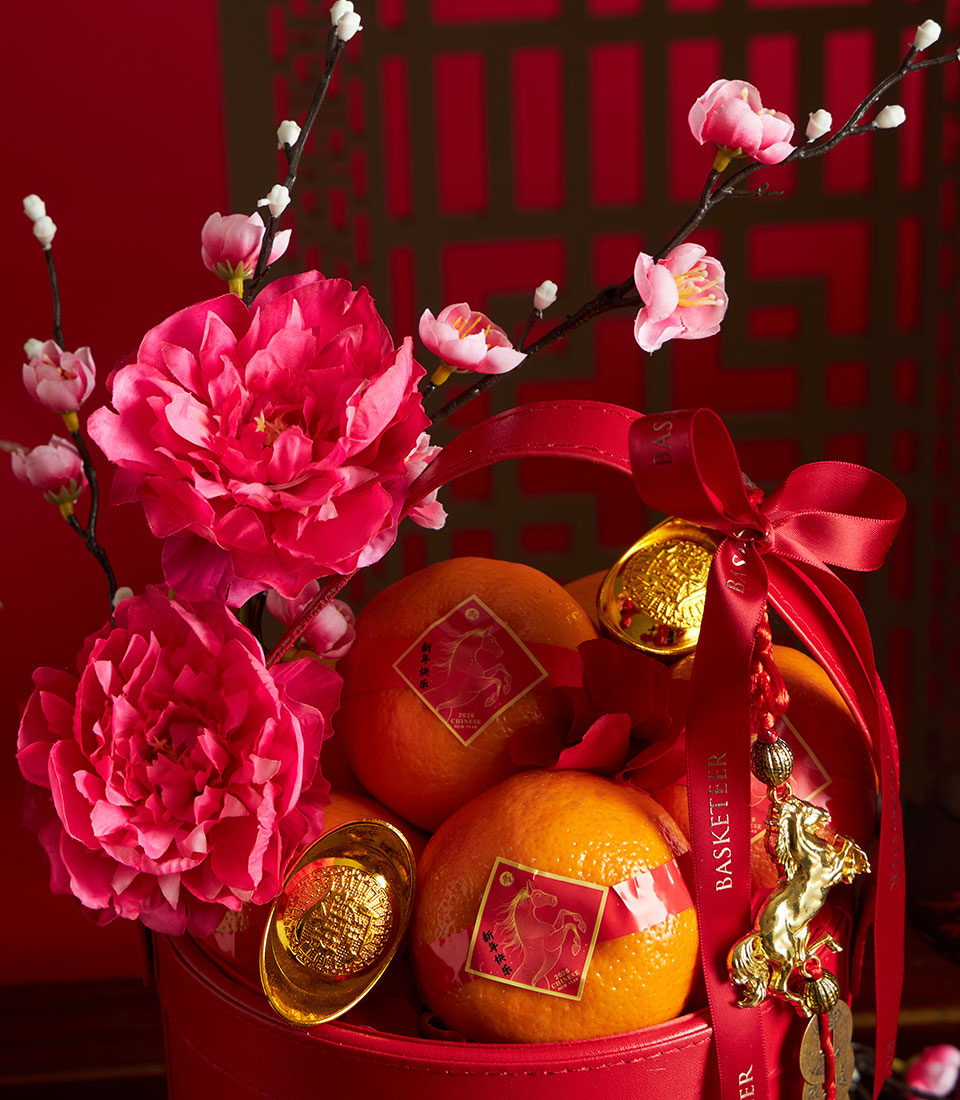 Vibrant red gift basket with mandarin oranges, golden horse charms, and pink artificial flowers for Chinese New Year