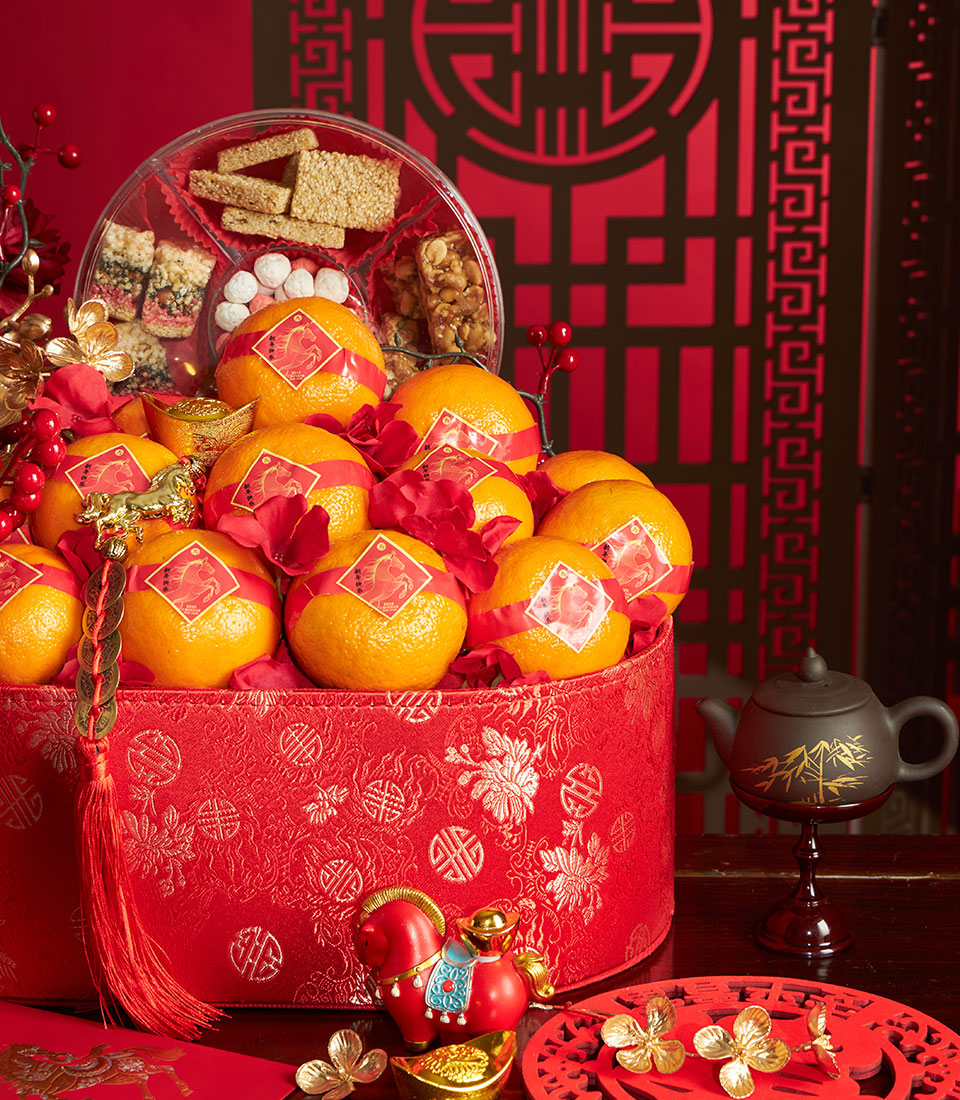 Lucky red Chinese New Year hamper with mandarin oranges, traditional snacks, and fresh flowers in gold-accented gift box
