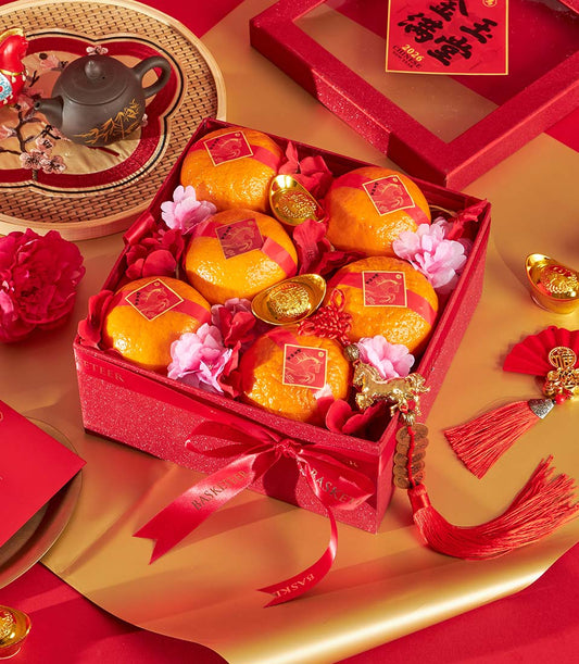 Festive red glitter gift box with mandarin oranges, gold ingots, and red satin ribbon for Chinese New Year