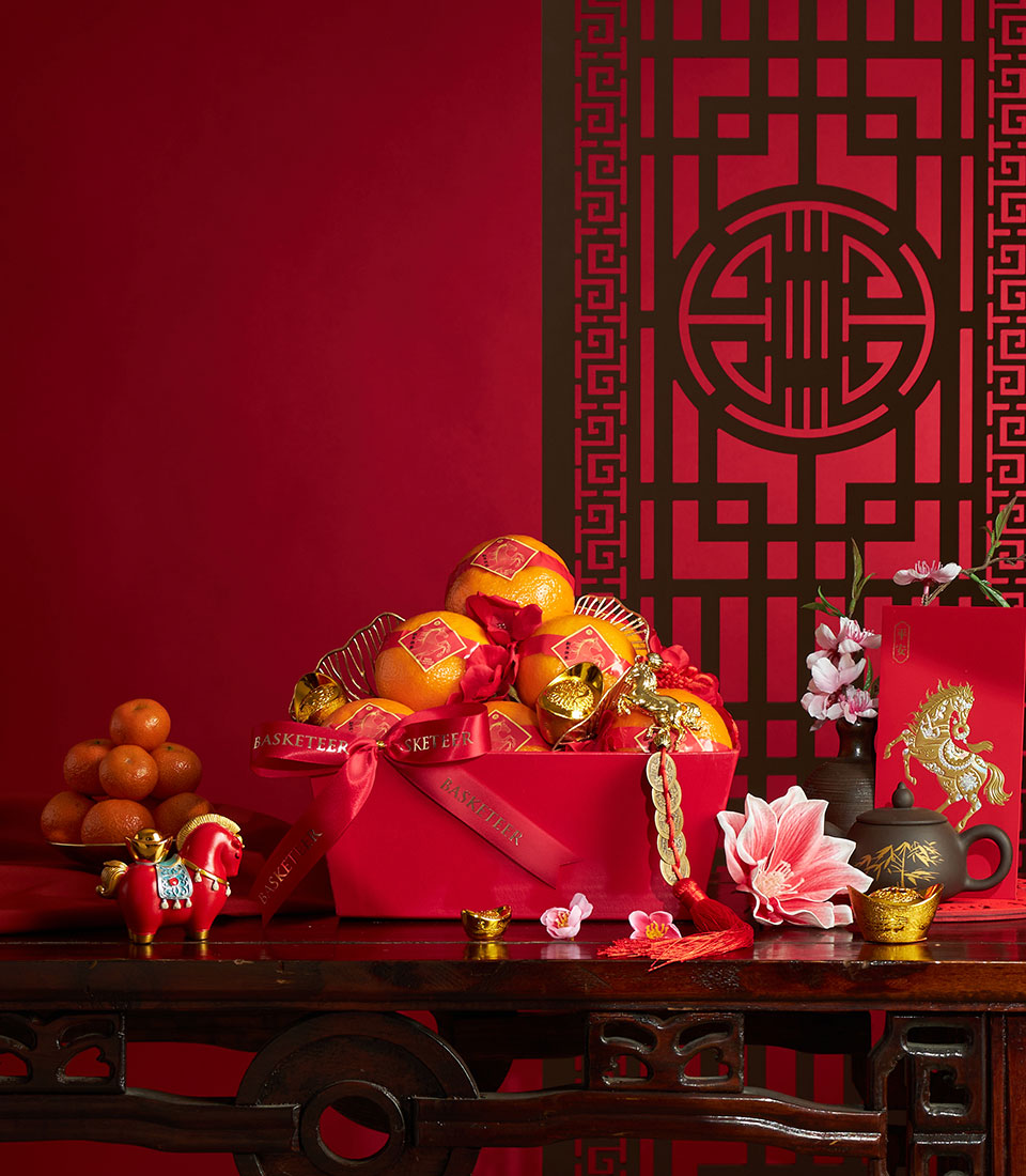 Mandarin orange gift box with gold ribbons and red satin wrap, surrounded by ceramic horse figurine, red envelope, cherry