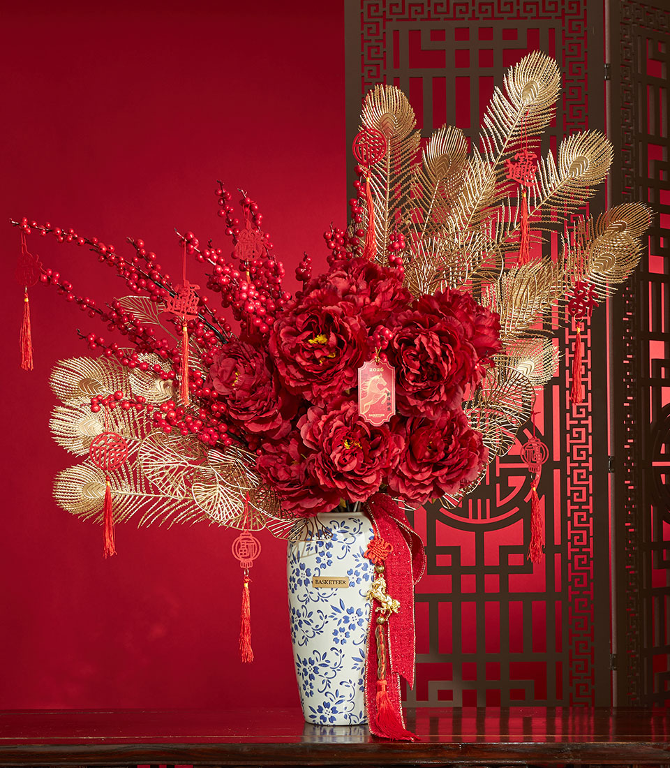 Deep red peony artificial flowers with peacock feathers and gold tassels in blue ceramic vase, Chinese New Year arrangement