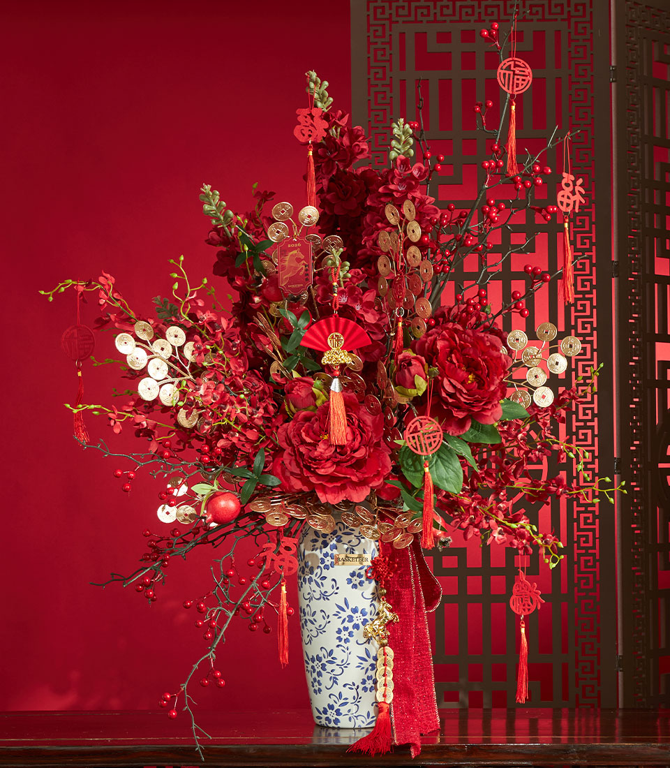 Basketeer premium hamper delivery Thailand: a luxurious Chinese New Year gift with red peonies, gold coin accents, and festive tassels in a blue-and-white vase.